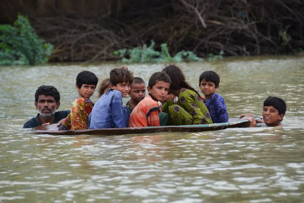 A man (L) along with a youth use a satellite dish to move children across a flooded area after heavy monsoon rainfalls in Jaffarabad district, Balochistan Province, Pakistan, on Aug. 26, 2022. (Fida Hussain/AFP via Getty Images)