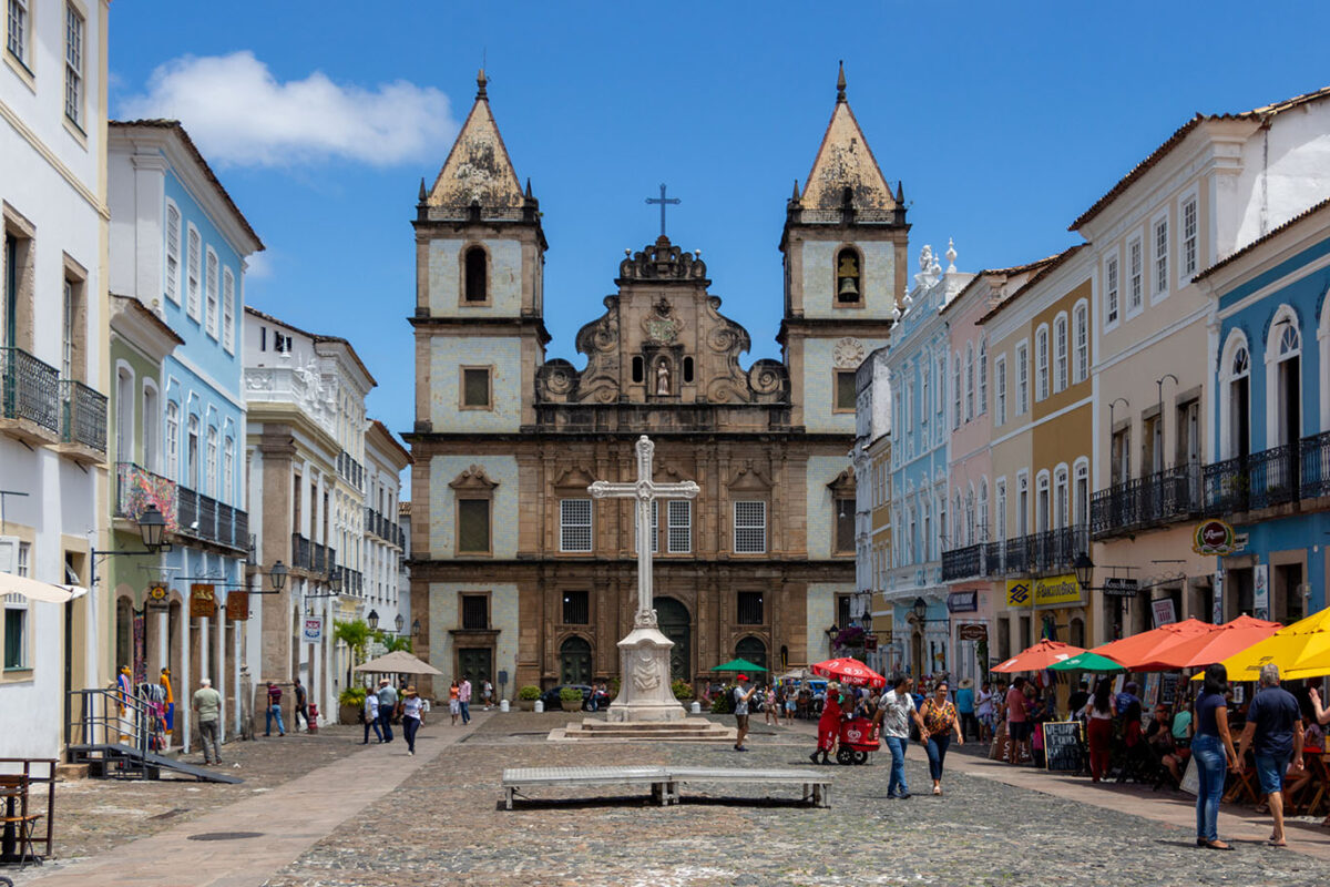 Among the colorful colonial buildings of Salvador, in the Brazilian state of Bahia, sits the church and convent of São Francisco, a church managed by Franciscan friars. The church is across the square from Cruzeiro de São Francisco, a large stone cross. Three doorways lead inside, with two bell towers on each side, on façades of white Brazilian sandstone. The upper middle façade has volutes (spirals), a white marble statue of St. Francis of Assisi, and the coat of arms of the Franciscan order. The overall façade is influenced by Mannerist architecture, an Italian artistic style from the late Renaissance. (Wellington Da Costa Gomez, CC BY-SA 4.0 , via Wikimedia Commons)