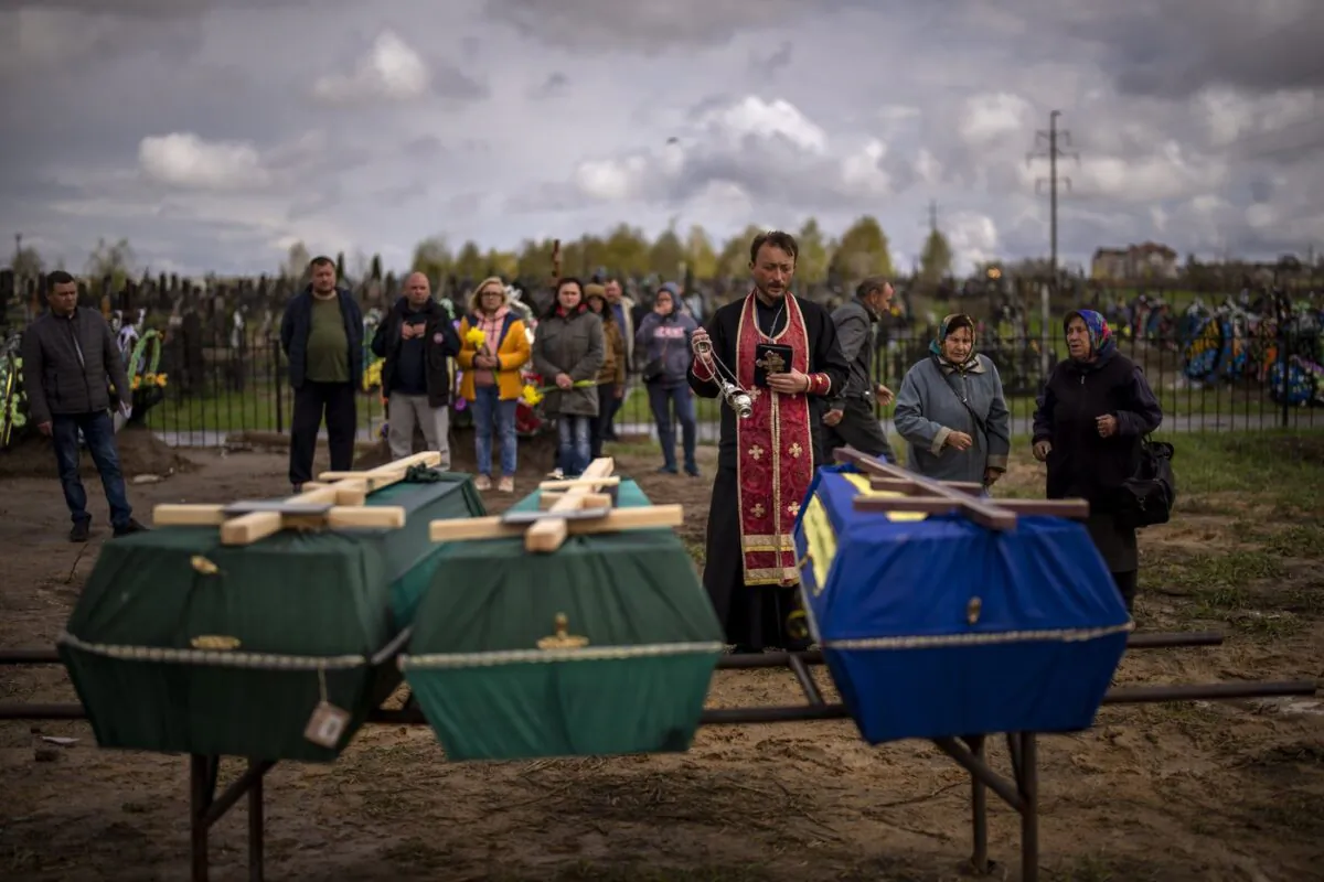 A priest blesses the remains of three people who died during the Russian occupation and were disinterred from temporary burial sites in Bucha, on the outskirts of Kyiv, on April 27, 2022. (AP/Emilio Morenatti)