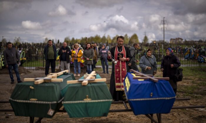 A priest blesses the bodies of three people who died during the Russian occupation and were transported from a temporary burial site in Bucha, a suburb of Kyiv, on April 27, 2022.  (AP/Emilio Morenatti)