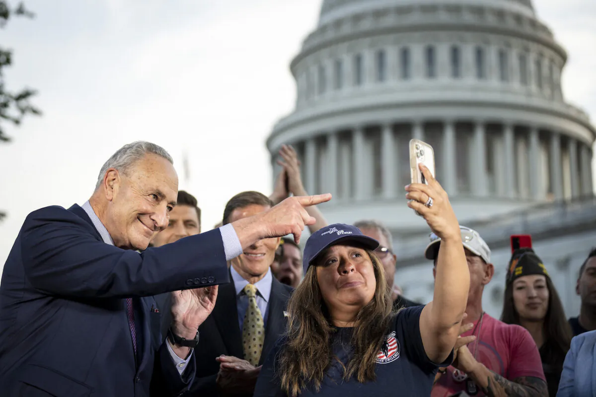 Senate Majority Leader Chuck Schumer (D-NY) looks on as Rosie Torres, wife of veteran Le Roy Torres who suffers from illnesses related to his exposure to burn pits in Iraq, holds up her husband Le Roy on her phone after the Senate passed the PACT Act at the U.S. Capitol in Washington, on Aug. 2, 2022. (Drew Angerer/Getty Images)