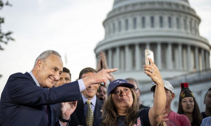 Senate Majority Leader Chuck Schumer (D-NY) looks on as Rosie Torres, wife of veteran Le Roy Torres who suffers from illnesses related to his exposure to burn pits in Iraq, holds up her husband Le Roy on her phone after the Senate passed the PACT Act at the U.S. Capitol in Washington, on Aug. 2, 2022. (Drew Angerer/Getty Images)