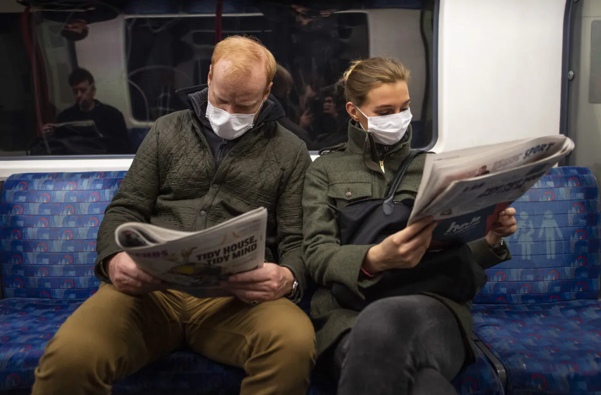 A couple sit on the Central Line Tube wearing protective masks while reading newspapers, in London on March 19, 2020. (Photo by Justin Setterfield/Getty Images)