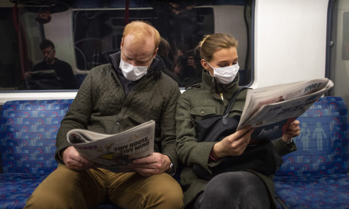 A couple sit on the Central Line Tube wearing protective masks while reading newspapers, in London on March 19, 2020. (Photo by Justin Setterfield/Getty Images)