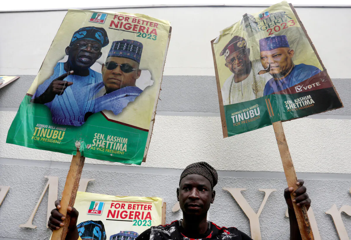 A supporter of Nigeria's All Progressive Congress (APC) ruling party holds posters of APC presidential and vice-presidential candidates outside a party meeting in Abuja on July 20, 2022. (Photo by Kola Sulaimon / AFP via Getty Images)