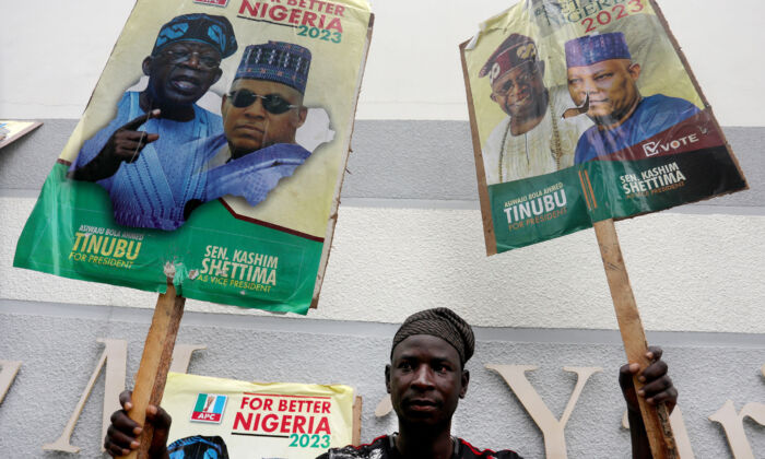 A supporter of Nigeria's All Progressive Congress (APC) ruling party holds posters of APC presidential and vice-presidential candidates outside a party meeting in Abuja on July 20, 2022. (Photo by Kola Sulaimon / AFP via Getty Images)