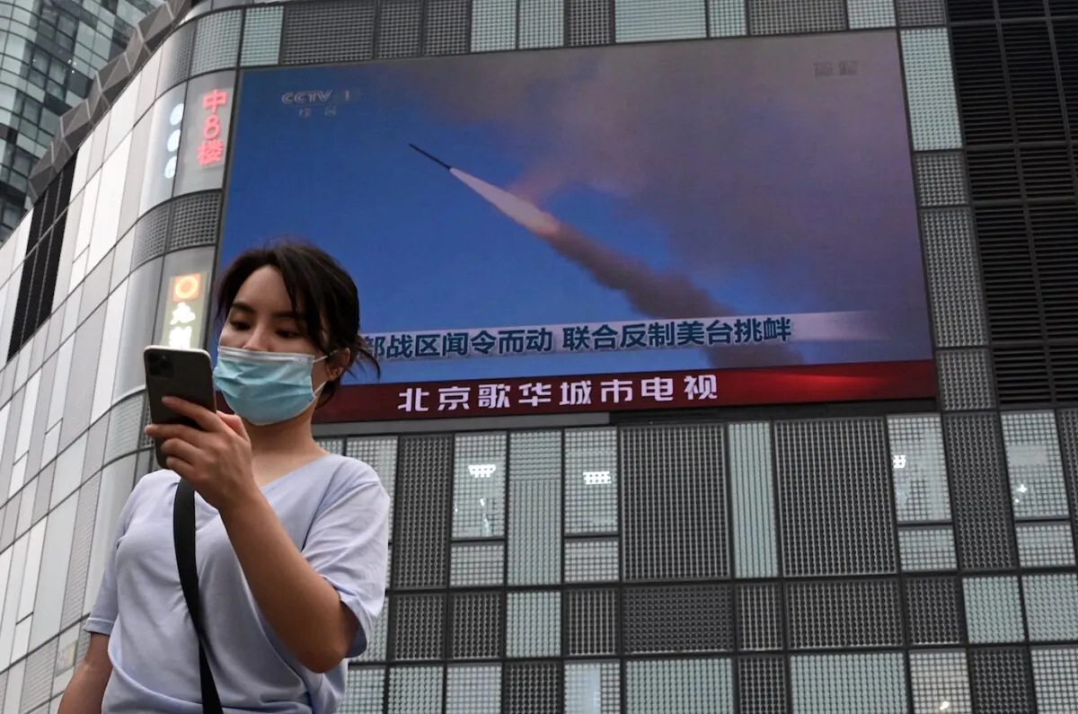 A woman uses her mobile phone as she walks in front of a large screen showing a news broadcast about China's military exercises encircling Taiwan, in Beijing on Aug.4, 2022. (Noel Celis/AFP via Getty Images)