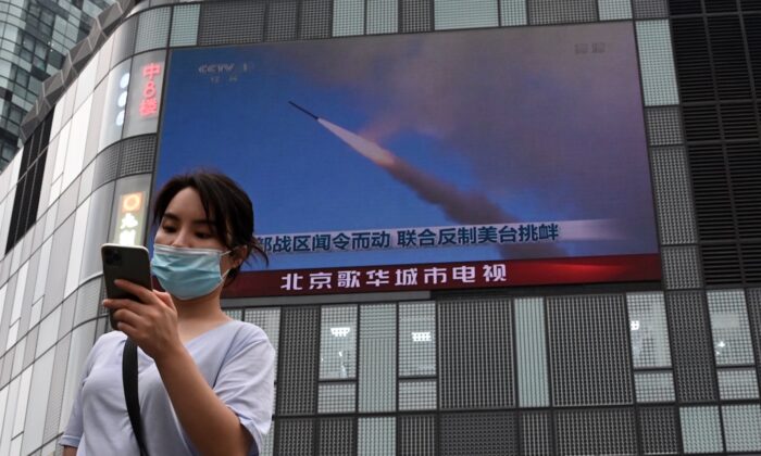 A woman uses her mobile phone as she walks in front of a large screen showing a news broadcast about China's military exercises encircling Taiwan, in Beijing on Aug.4, 2022. (Noel Celis/AFP via Getty Images)