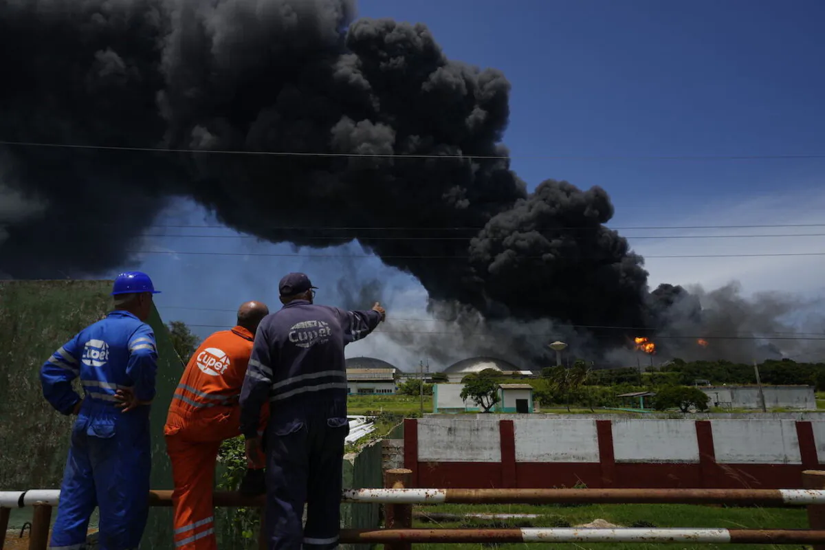 Workers of the Cuba Oil Union, known by the Spanish acronym CUPET, watch a huge rising plume of smoke from the Matanzas Supertanker Base, as firefighters work to quell a blaze which began during a thunderstorm the night before, in Matazanas, Cuba, on Aug. 6, 2022. (Ramon Espinosa/AP Photo)
