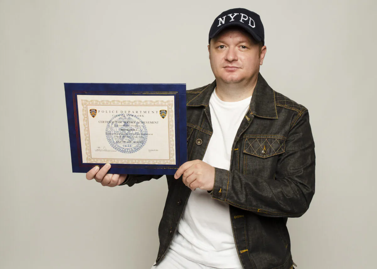 Unvaccinated and terminated NYPD police officer Marjel Kola, with his "Cop of the Month" certificate of service achievement on August 8, 2022. (Dave Paone/The Epoch Times)
