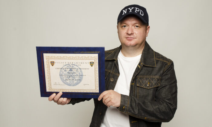 Unvaccinated and terminated NYPD police officer Marjel Kola, with his "Cop of the Month" certificate of service achievement on August 8, 2022. (Dave Paone/The Epoch Times)