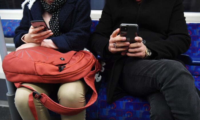 A close-up of an unidentifiable man and woman sitting next to each other on the Tube, both looking at their phones. ((Kirsty O’Connor/PA Media)


