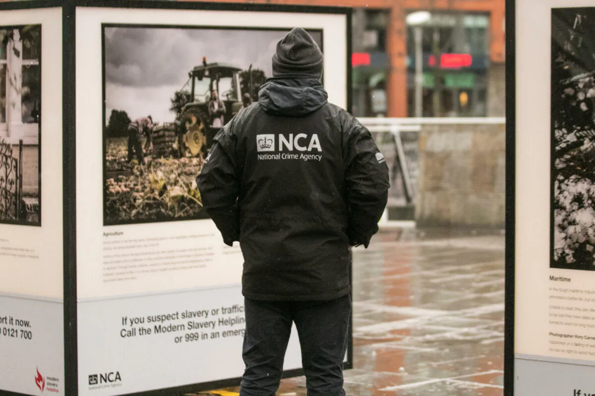 An undated image of an NCA officer in front of a poster highlighting modern slavery. (Alamy/PA)