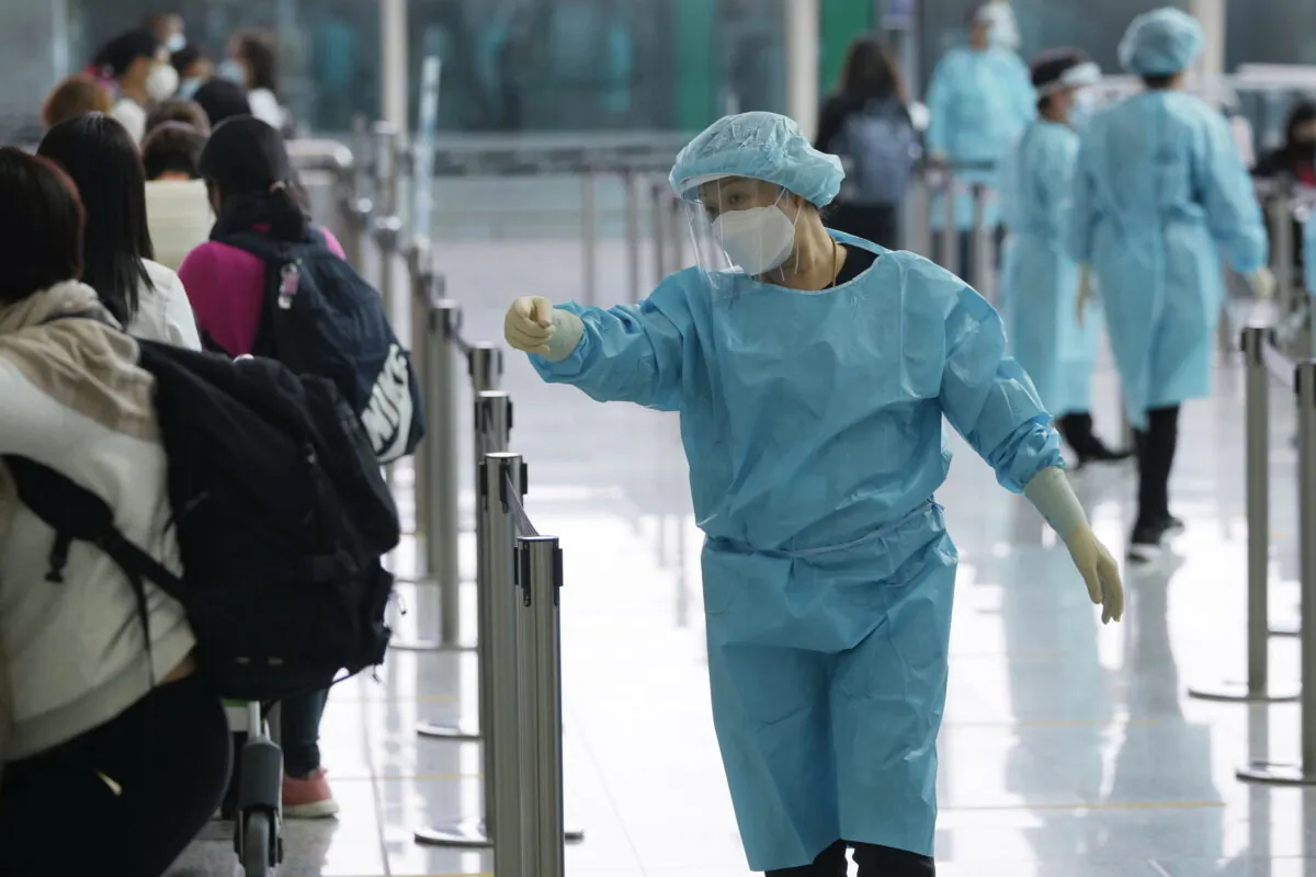Workers wearing protective gear direct arriving passengers to quarantine hotels in the Hong Kong International Airport in Hong Kong on April 1, 2022. (Kin Cheung/AP Photo)