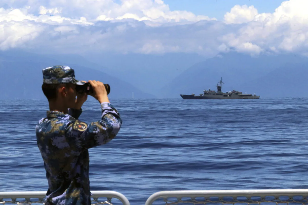 A People's Liberation Army member looks through binoculars during military exercises as Taiwan's frigate Lan Yang is seen in the background on Aug. 5, 2022. (Lin Jian/Xinhua via AP)