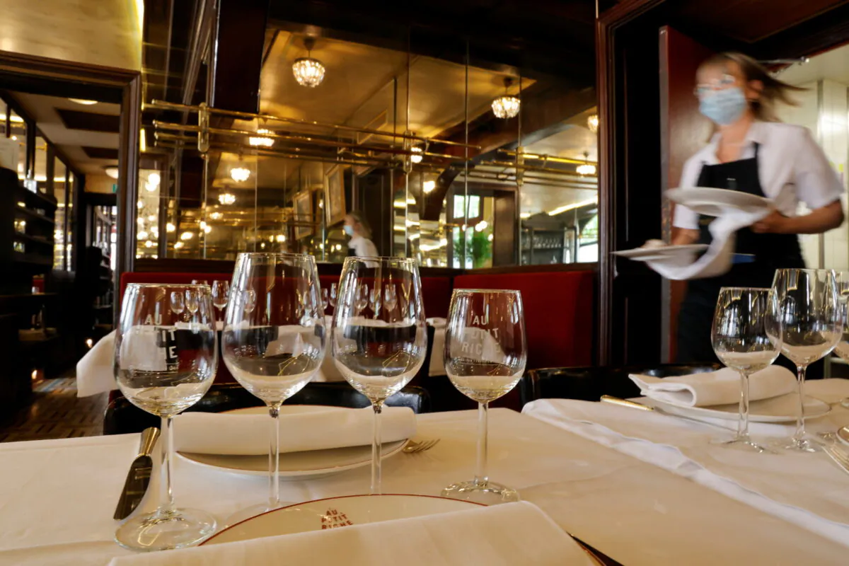 A waiter serves dishes in a dining room at Au Petit Riche restaurant in Paris as cafes, bars and restaurants reopen indoor dining rooms with a fitted gauge and health protocol after closing down for months amid the COVID-19 outbreak on June 9, 2021. (Pascal Rossignol/Reuters)