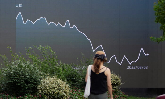 A pedestrian walks past a giant display showing a stock graph, in Shanghai, China, on Aug. 3, 2022. (Aly Song/Reuters)