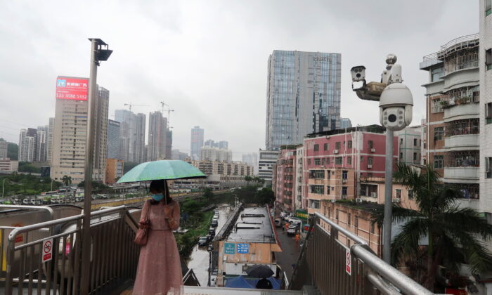 A woman holding an umbrella walks on a pedestrian bridge by surveillance cameras, near Caopu in Shenzhen's Luohu district, Guangdong province, China, on July 5, 2022. (David Kirton/Reuters)