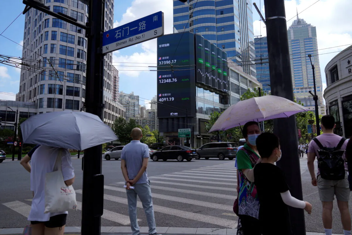 Pedestrians wait to cross a road at a junction near a giant display of stock indexes in Shanghai, China, on Aug. 3, 2022. (Aly Song/Reuters)