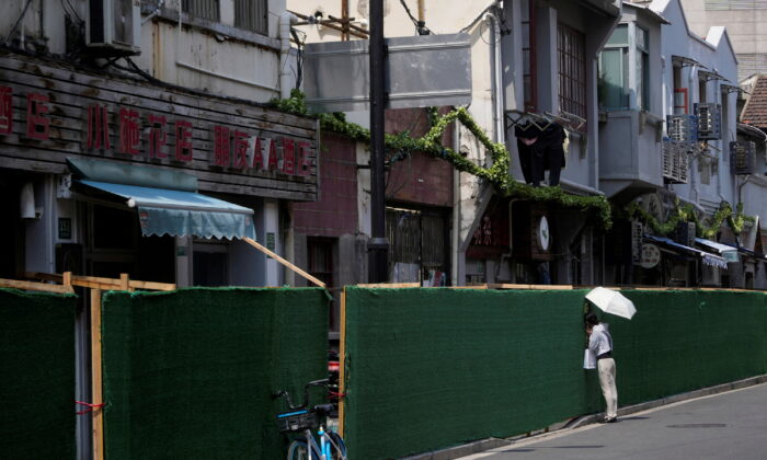 A woman looks in through a gap in a barrier at a residential area, amid new lockdown measures in parts of the city to curb the COVID-19 outbreak in Shanghai, on July 11, 2022. (Aly Song/Reuters)