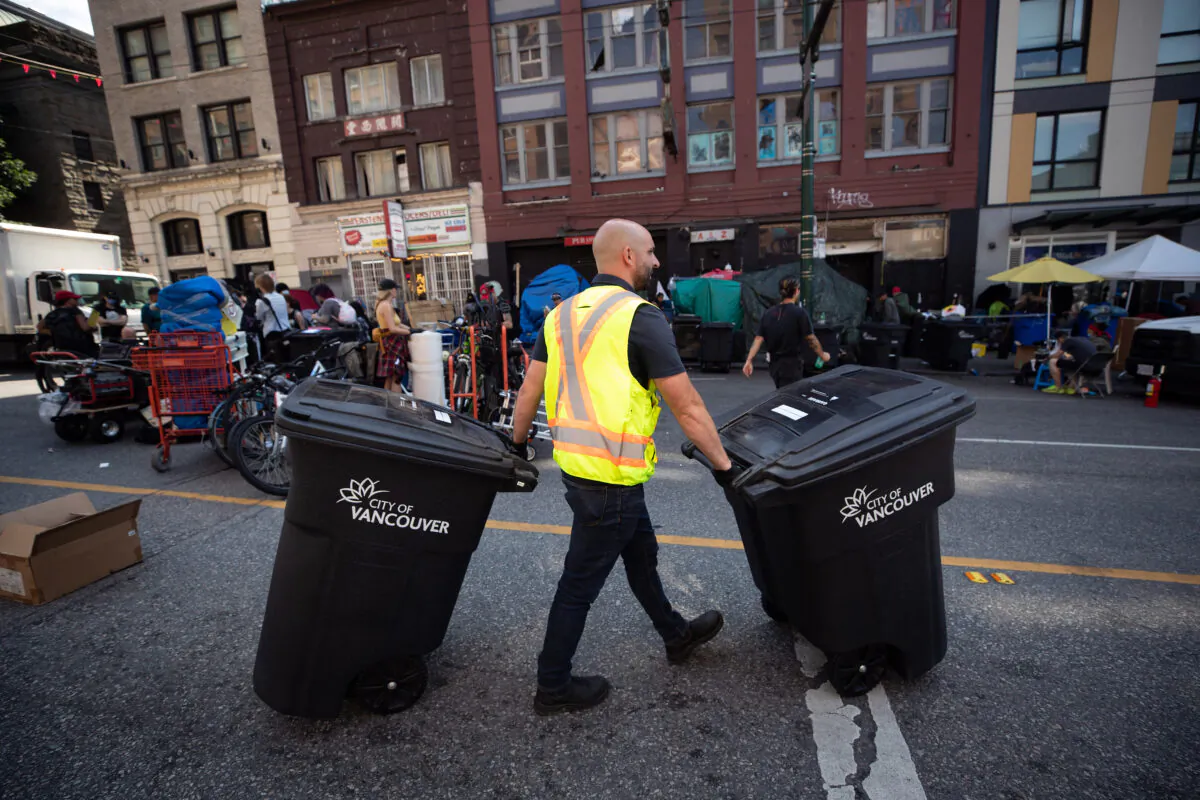 A worker moves garbage bins as the city works to clear tents from the sidewalk at a sprawling homeless encampment on East Hastings Street in the Downtown Eastside of Vancouver, on Aug. 9, 2022. (The Canadian Press/Darryl Dyck)