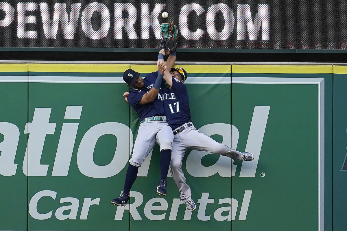 Seattle Mariners center fielder Julio Rodriguez, left, and right fielder Mitch Haniger collide at the wall while trying to catch a fly ball from Los Angeles Angels' Luis Rengifo during the first inning of a baseball game Monday, Aug. 15, 2022, in Anaheim, Calif. Rengifo was awarded a solo home run on the play. (AP Photo/Marcio Jose Sanchez)
