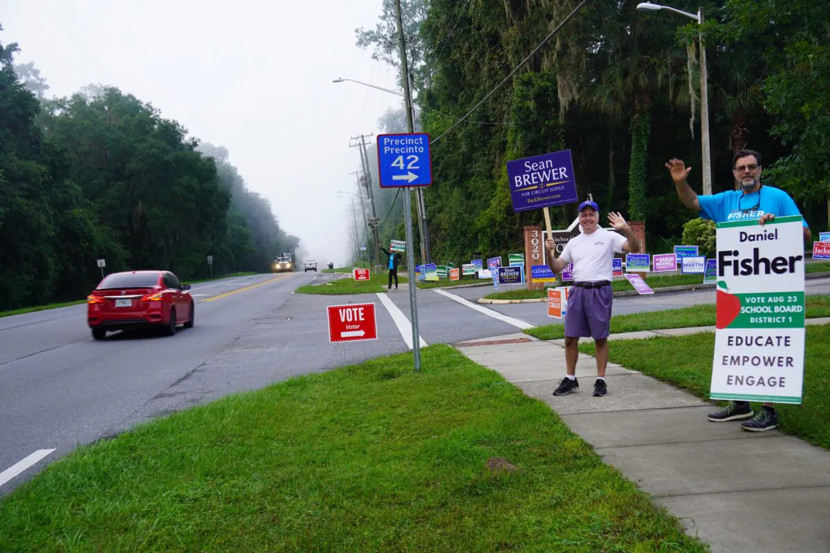 Campaign volunteers Steven Ward (R) and and Brian Ray wave at cars passing a voting sit in Gainesville, Fla., on Aug. 23. (Nanette Holt/The Epoch Times)