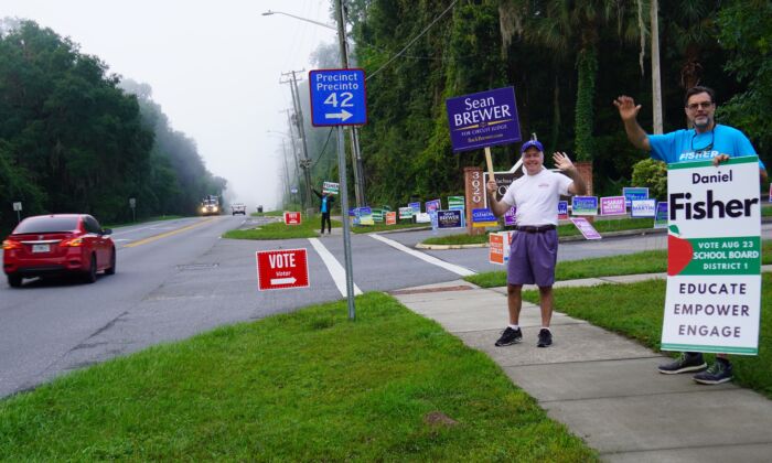 Campaign volunteers Steven Ward (R) and and Brian Ray wave at cars passing a voting sit in Gainesville, Fla., on Aug. 23. (Nanette Holt/The Epoch Times)
