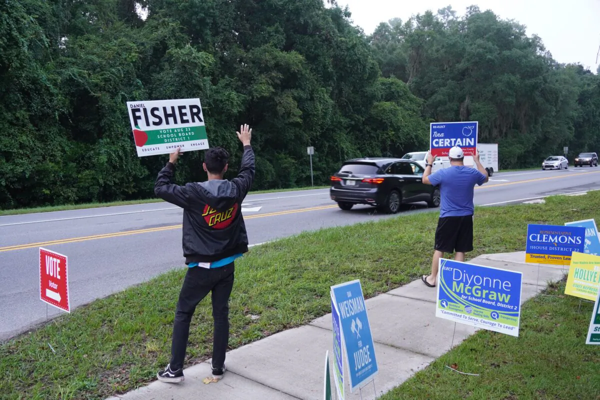 Volunteers for opposing school board candidates in a heated race in Alachua County wave to passing cars outside a Gainesville, Fla. voting site on Aug. 23, 2022. (Nanette Holt/The Epoch Times)