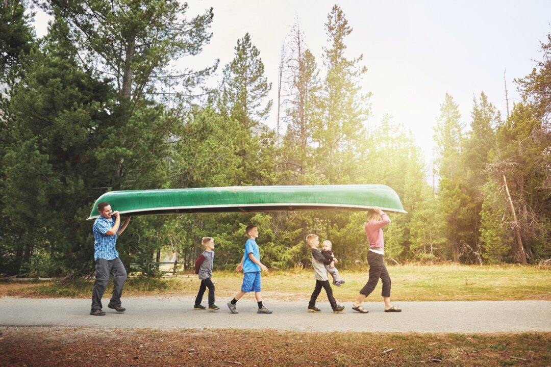 A family uses teamwork to carry their canoe to the water's edge at Jenny Lake, GTNP, WY.