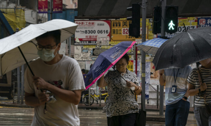 People holding umbrellas under strong wind walk past a crosswalk as tropical storm Ma-on passes Hong Kong on Aug. 25, 2022. (Anthony Kwan/AP Photo)