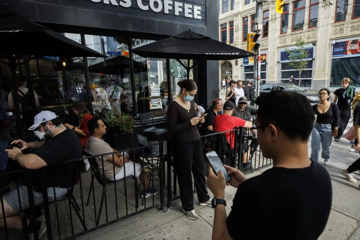 People use electronics outside a coffee shop in Toronto amid a nationwide Rogers outage, affecting many of the telecommunication company's services, July 8, 2022. (The Canadian Press/Cole Burston)