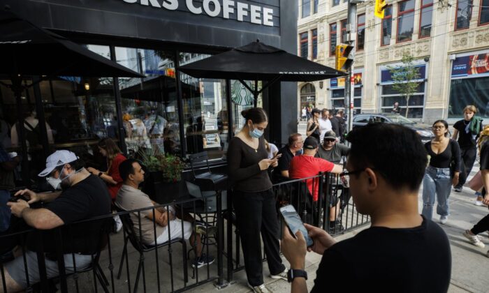 People using electronic devices outside coffee shops in Toronto, July 8, 2022, after a nationwide Rogers power outage has affected the services of many telecom companies.  (The Canadian Press/Cole Burston)