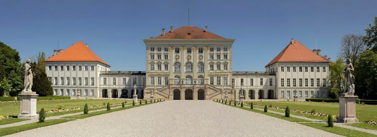 A long and wide walkway invites visitors to admire the front façade of Nymphenburg Palace. Given as a gift to the electress Henriette Adelaide, the property was originally a country estate, to be used as a hunting lodge. The electress planned to make the palace her own by holding court in a mythological setting, dressed as the goddess Diana, but she died before her plans were realized. Her villa, the central structure today, consisted of a two-story cube, with a garden and a large wood behind the building. Over the years, the building was extended, but very few alterations were made to the original structure. In 1715, architect Joseph Effner created two wings on each side of the palace and modernized the façade in a French style. The central building has details from the French Regency style, an architectural and design transitional style between the architectural styles promulgated by Louis XIV and Louis XV. (Richard Bartz/CC BY-SA 2.5)
