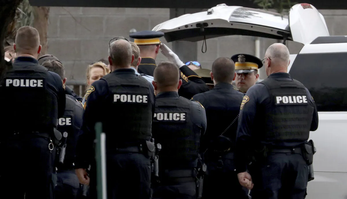 Tucson Police officers stand with an an honor guard as the body of Pima County Constable Deborah Martinez-Garibay is loaded into a Pima County Medical Examiner van for transport from the scene at the Lind Commons Apartments in Tucson, Ariz., on Aug. 27, 2022. (Kelly Presnell/Arizona Daily Star via AP)