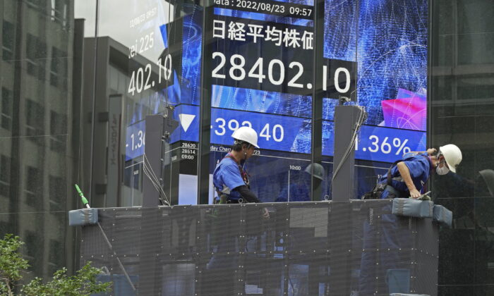 Window cleaners prepare their work in front of an electronic stock board showing Japan's Nikkei Index at a securities firm, on Tuesday,  Aug. 23, 2022, in Tokyo. Asian shares are trading lower Tuesday, echoing a broad sell-off on Wall Street amid speculation about another interest rate raise from the U.S. Federal Reserve. (AP Photo/Eugene Hoshiko)