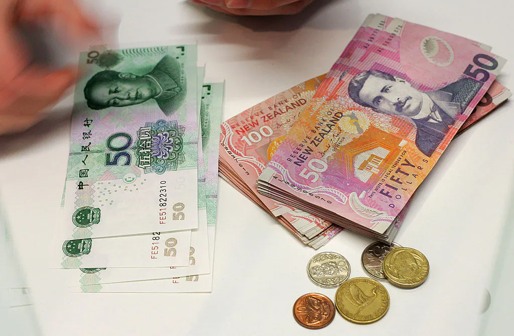 A currency exchange teller counts out Chinese Yuan alongside a stack of New Zealand dollars and coins in Auckland, New Zealand, on 21 April, 2007. (Dean Treml/AFP via Getty Images)