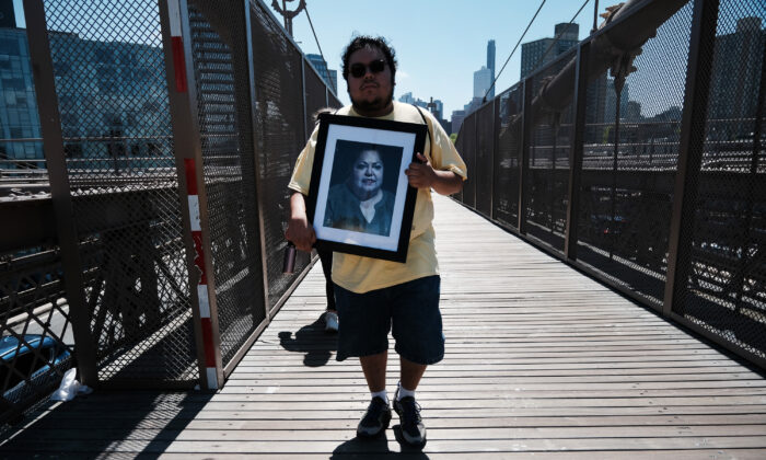 Austin Aragon holds a picture of his mother Valarie as he joins others heading across the Brooklyn Bridge while participating in the second annual COVID March to Remember, in New York, on Aug. 6, 2022. The march was held across dozens of cities to raise awareness about pandemic needs. (Spencer Platt/Getty Images)