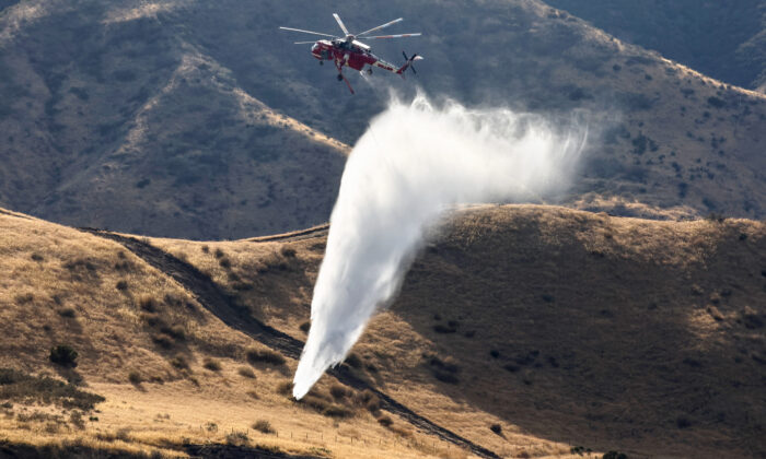 A firefighting helicopter drops water as firefighters stand near a hotspot a day after the Route Fire burned through the area near Castaic, Calif., on Sept. 1, 2022. (Mario Tama/Getty Images)