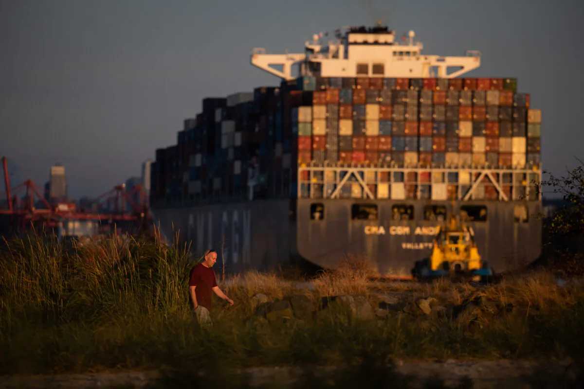 A man walks on Ambleside Beach as a container ship is guided into port by tugboats at sunset in West Vancouver, B.C., on Aug. 13, 2022. (Darryl Dyck/The Canadian Press)
