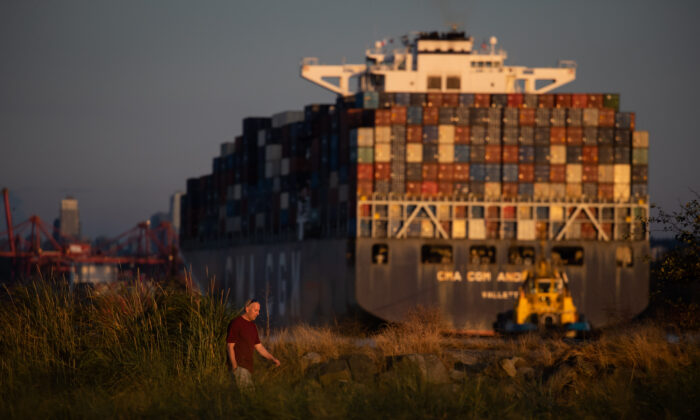 A man walks on Ambleside Beach as a container ship is guided into port by tugboats at sunset in West Vancouver, B.C., on Aug. 13, 2022. (Darryl Dyck/The Canadian Press)