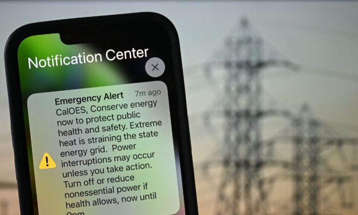 A photo illustration shows a background of electric power infrastructure with an Apple iPhone showing an Emergency Alert notification from CalOES urging the public to conserve energy to protect health and safety as the electricity grid is strained during a heat wave in Los Angeles, Calif., on Sept. 6, 2022. (Patrick T. Fallon/AFP via Getty Images)