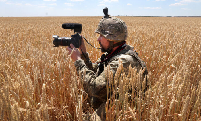 A Ukrainian military journalist takes cover in a wheat field as he captures video while a tank team with the 14th Mechanized Brigade of Prince Roman the Great fire on an enemy position in the Donetsk District, Ukraine, on July 1, 2022. (Scott Olson/Getty Images)
