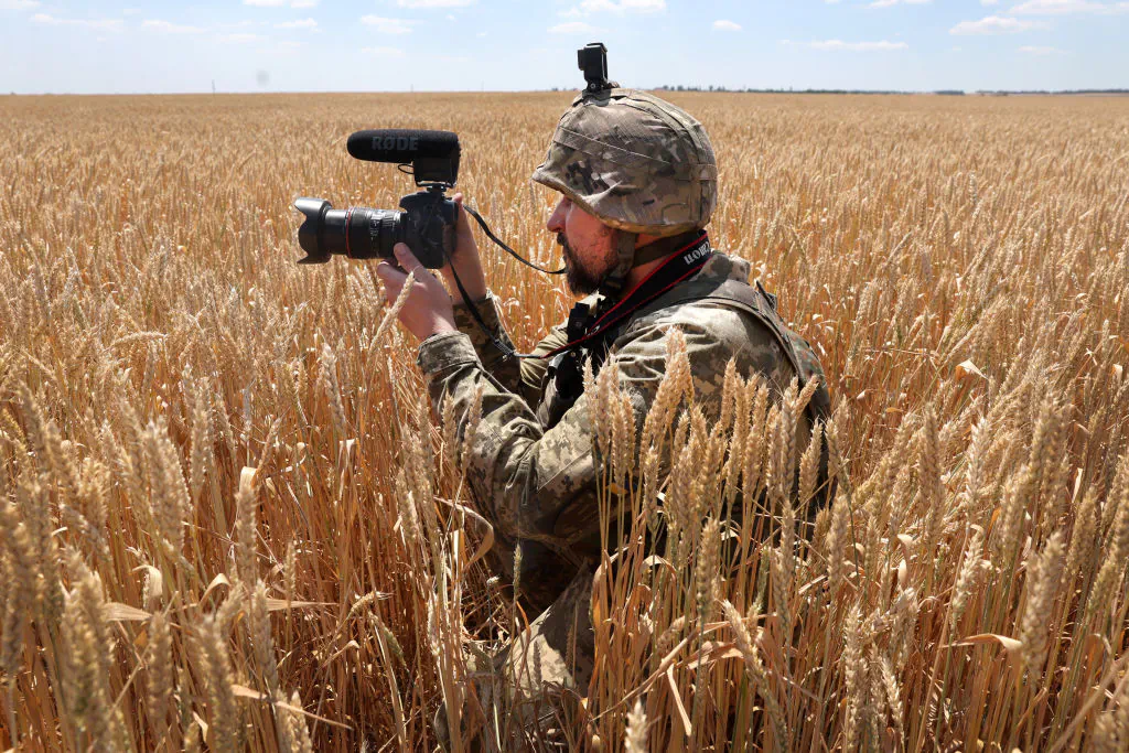 A Ukrainian military journalist takes cover in a wheat field as he captures video while a tank team with the 14th Mechanized Brigade of Prince Roman the Great fire on an enemy position in the Donetsk District, Ukraine, on July 1, 2022. (Scott Olson/Getty Images)