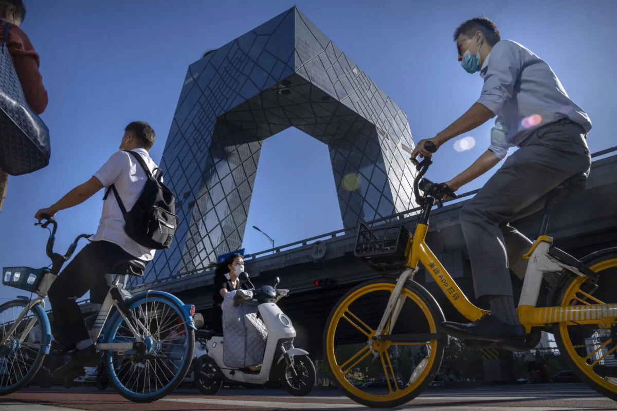 Commuters ride bicycles near the China Central Television (CCTV) building in the central business district in Beijing, Sept. 1, 2022. (AP Photo/Mark Schiefelbein)