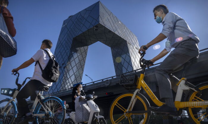 Commuters wearing face masks ride bicycles near the China Central Television (CCTV) building in the central business district in Beijing, on Sept. 1, 2022. (Mark Schiefelbein/AP Photo)