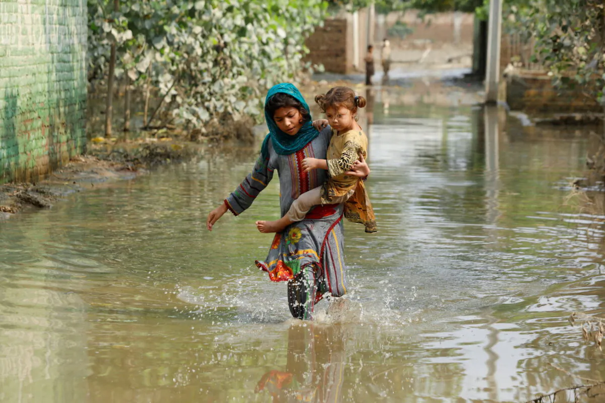A girl carries her sibling as she walks through stranded flood water, following rains and floods during the monsoon season in Nowshera, Pakistan, on Sept. 4, 2022. (Fayaz Aziz/Reuters)