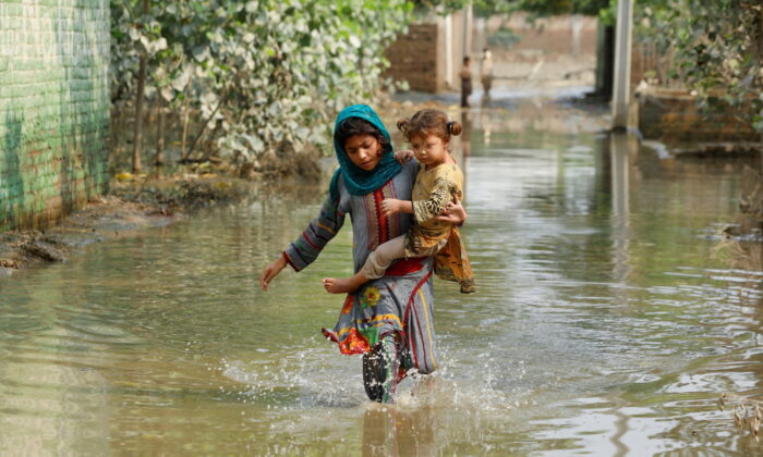 A girl carries her sibling as she walks through stranded flood water, following rains and floods during the monsoon season in Nowshera, Pakistan, on Sept. 4, 2022. (Fayaz Aziz/Reuters)