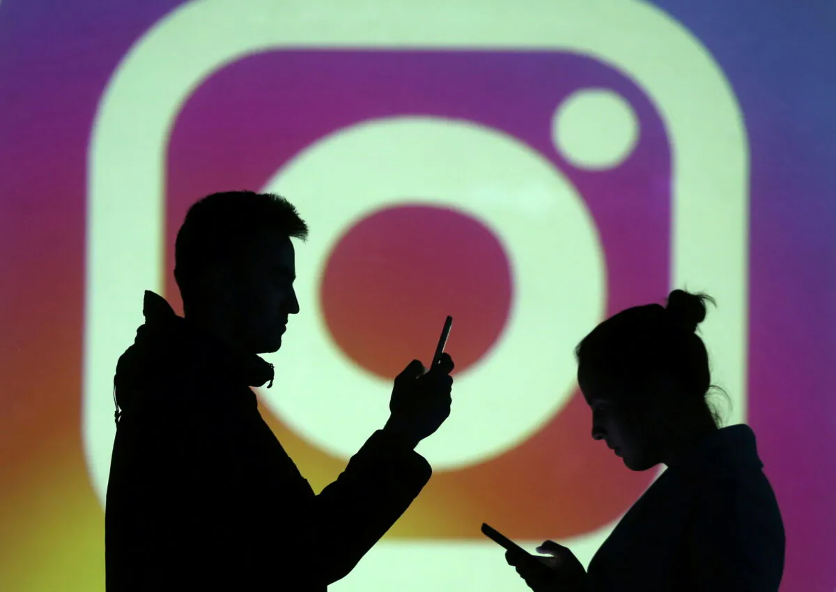 Silhouettes of mobile users are seen next to a screen projection of Instagram logo in this picture illustration taken March 28, 2018.  REUTERS/Dado Ruvic/Illustration