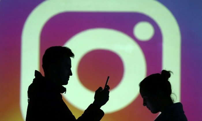 Silhouettes of mobile users are seen next to a screen projection of Instagram logo in this picture illustration taken on Mar. 28, 2018.  (Reuters/Dado Ruvic/Illustration)